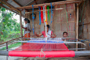 People weaving fabric on a loom in a rustic setting.