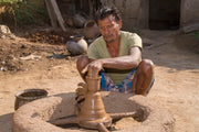 Man shaping clay on a pottery wheel outdoors