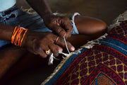 Hands tying fringe on a colorful woven rug